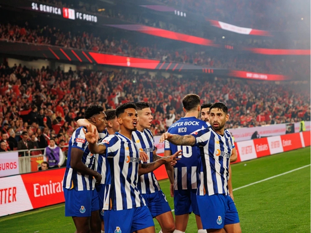 Top-Spiele der Liga Portugal – Sichern Sie sich Ihre Fanreise Die Mannschaft des FC Porto im blau-weiß gestreiften Trikot bejubelt gemeinsam ein Tor im gegnerischen Stadion vor einer vollbesetzten, rot leuchtenden Tribüne.